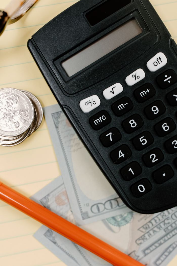 About Black calculator, coins, and cash on a yellow notepad with a pencil.