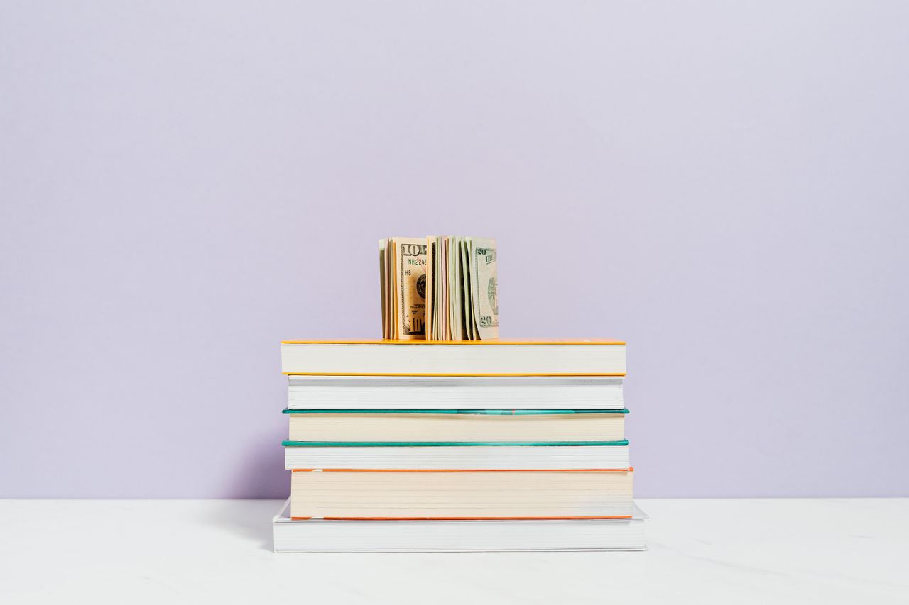Mastering the First Impression: Your intriguing post title goes here Stack of books with a stack of US dollar bills on top against a pastel background.
